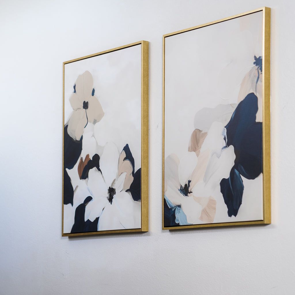 The Floral Serenity Set of 2 features minimalist abstract floral wall art in neutral and dark blue tones, displayed in gold-colored frames—perfect for adding elegance to your living room decor.