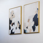 The Floral Serenity Set of 2 features minimalist abstract floral wall art in neutral and dark blue tones, displayed in gold-colored frames—perfect for adding elegance to your living room decor.