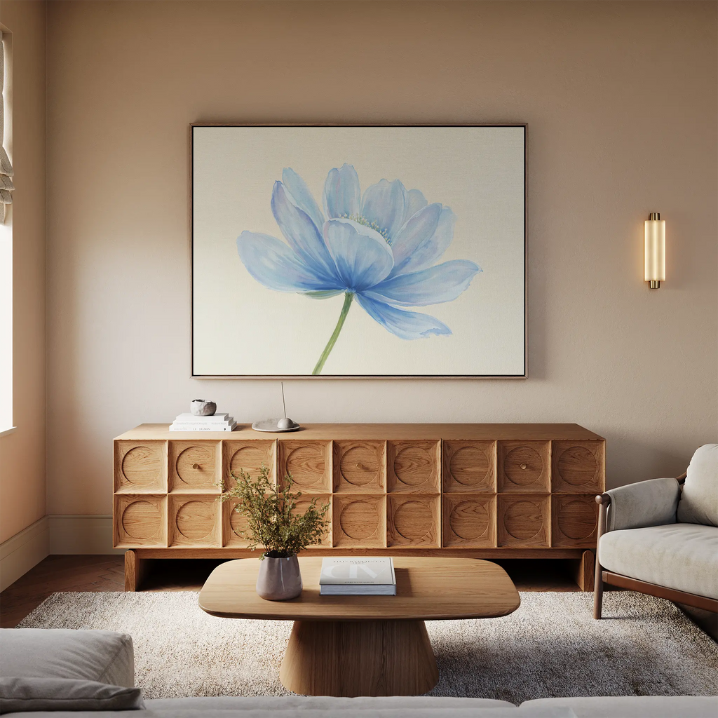 A modern living room with a light wood sideboard, a beige sofa, wooden coffee table with flowers, and the Daybreak Flower Canvas Art as minimalist wall decor above the sideboard, all illuminated by soft natural window light.