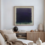 A modern living room features a beige sofa with neutral cushions, a wooden sideboard with books and vases, and the striking Deepest Night Canvas Art in dark blue and green as minimalist wall decor.