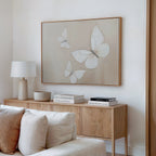 A minimalist living room with a light wood sideboard, white lamp, decorative bowl, stacked books, and Delicate Whites Canvas Art above a cream sofa adds Nordic Park charm and sophisticated neutral wall decor.