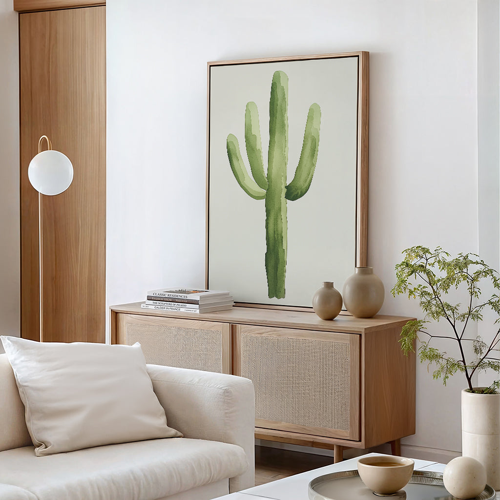 A modern minimalist living room features a beige sofa, light wood sideboard, and Desert Cactus Canvas Art on the wall. Neutral vases, books, and a small green plant provide simple decorative touches to complete the look.