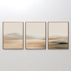 The Desert Haze Set of 3 features minimalist wall art prints in gold frames with soft, blurred beige and brown tones, suggesting a serene landscape—ideal for living room decor displayed side by side on a white wall.
