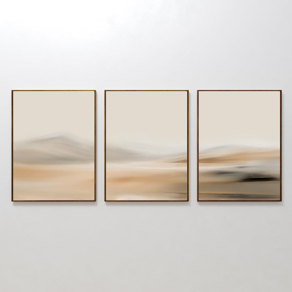 The Desert Haze Set of 3 features minimalist wall art prints in gold frames with soft, blurred beige and brown tones, suggesting a serene landscape—ideal for living room decor displayed side by side on a white wall.