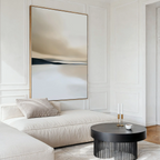 A modern living room features a cream sofa, a round black coffee table with candles and a cup, and the Desert Quietude Canvas Art – Vertical above the sofa. Neutral tones and minimalist decor create an inviting, serene space.