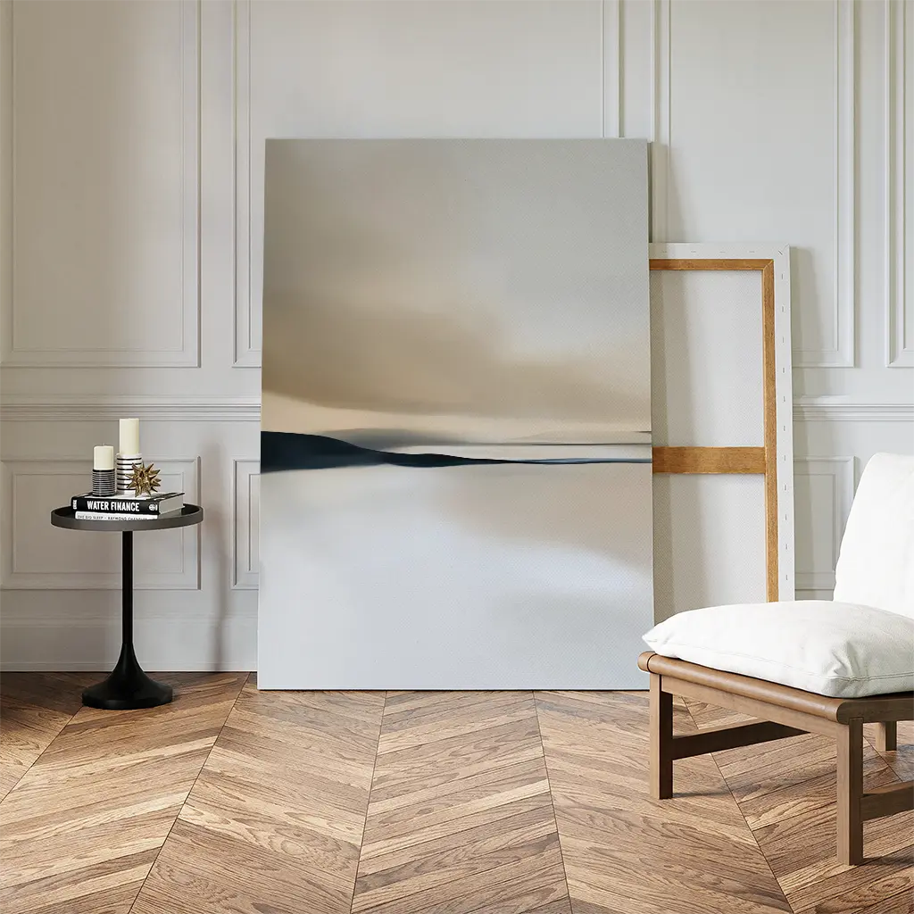A minimalist living space with herringbone wood floors showcases the Desert Quietude Canvas Art – Vertical against a white-paneled wall. A small round table with candles and books and a modern chair complete the stylish decor.