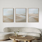 A modern living room with a light beige curved sofa, a round wooden coffee table, and the Desert Serenity Set of 3 minimalist wall art in soft neutral tones displayed above the sofa.