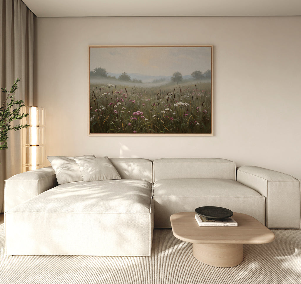 A modern living room with a light beige sectional sofa, wooden coffee table, tall glass lamp, potted plant, and nature-inspired wall art—a large framed Distant Fields Canvas Art—on the wall.