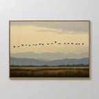 Bring Nordic Park serenity to your space with the Distant Flight Canvas Art, featuring flying birds in a V-formation above grassy fields, distant trees, and layered blue-gray mountains beneath a cloudy sky.