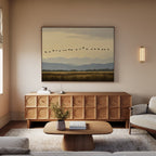 A cozy living room with neutral tones includes a wooden sideboard, low coffee table with a vase of flowers, sofa, and a striking Distant Flight Canvas Art print depicting birds flying over mountains and fields.