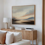 A cozy living room with a light wood sideboard, neutral decor, books, a white lamp, and minimalist wall art—a large Distant Peaks Canvas Art—hanging above the furniture on a white wall.