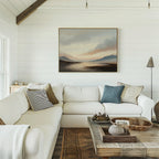 A cozy white living room with a large sectional, textured pillows, and rustic wooden coffee table features the Distant Peaks Canvas Art of mountains and water on shiplap walls. Warm natural light enhances the inviting decor.