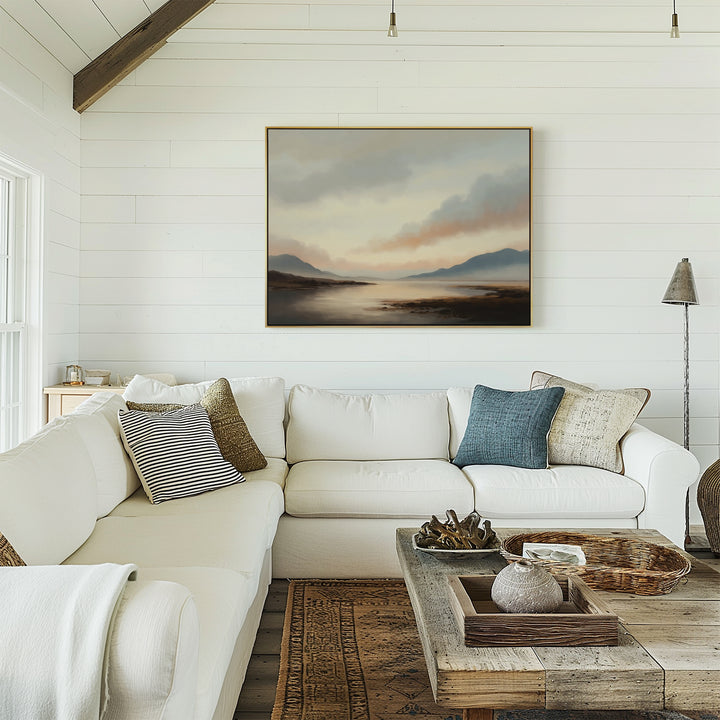 A cozy white living room with a large sectional, textured pillows, and rustic wooden coffee table features the Distant Peaks Canvas Art of mountains and water on shiplap walls. Warm natural light enhances the inviting decor.