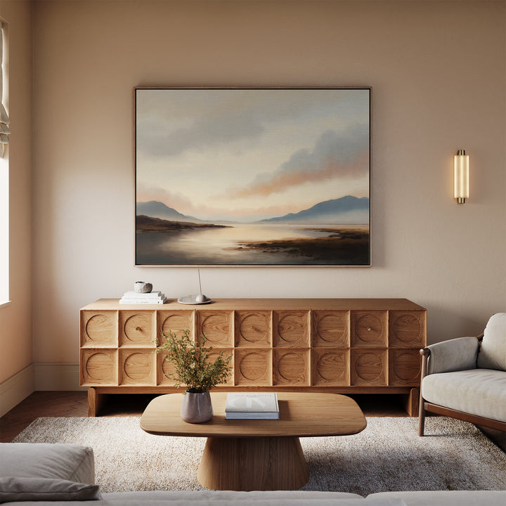 A modern living room features a light wood sideboard topped with the Distant Peaks Canvas Art, a low coffee table, beige sofa, and warm lighting; neutral tones create a calm, inviting space.