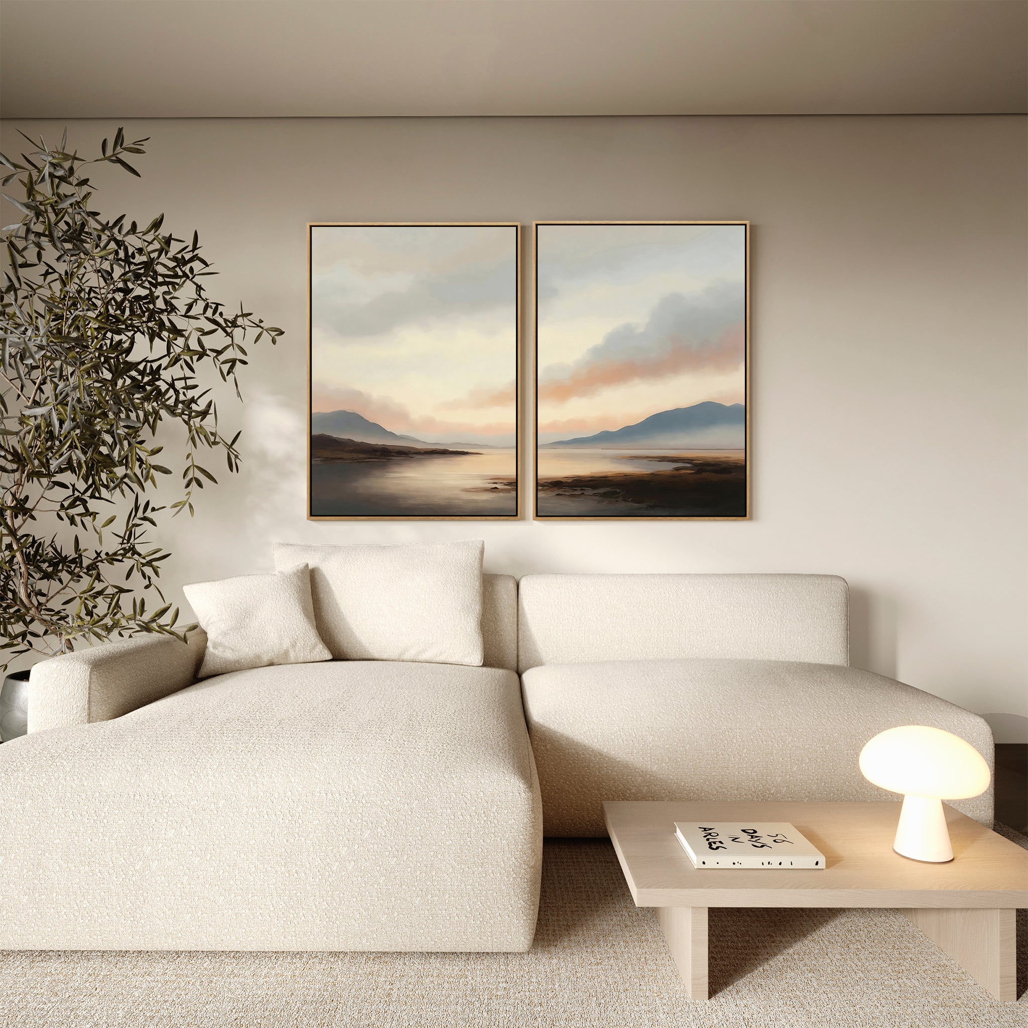 A minimalist living room with a textured cream sectional sofa, a small wooden table featuring a glowing lamp and a book, a leafy plant, and the Distant Peaks Set of 2 minimalist wall art depicting mountains and a lake.