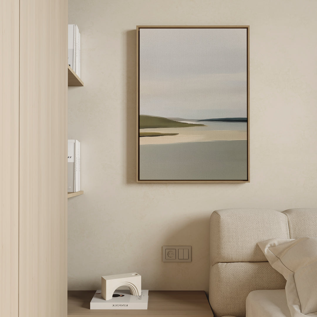 A minimalist living room corner features a beige couch, sage green accents, a wooden shelf with books, a geometric white sculpture, and the Distant Shores Canvas Art framed on a light-colored wall.