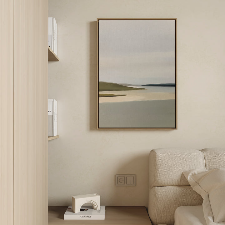A minimalist living room corner features a beige couch, sage green accents, a wooden shelf with books, a geometric white sculpture, and the Distant Shores Canvas Art framed on a light-colored wall.