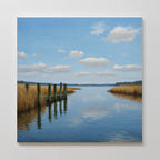 The Dockside Reflection Canvas Art features a serene river scene with wooden posts, golden grasses, and a blue sky, creating tranquil wall art with the peaceful landscape beautifully mirrored on the waters surface.