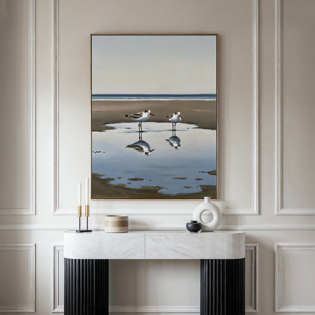 Drifted Calm Canvas Art featuring two seagulls by the water hangs on a beige wall above a modern console table, adding coastal vibes and minimalist style to your space.