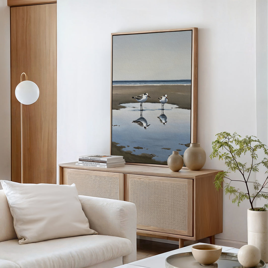 A modern living room with neutral tones, highlighting a wooden sideboard, ceramic vases, a small potted plant, and the Drifted Calm Canvas Art featuring two seagulls by the water—ideal for contemporary or coastal spaces.
