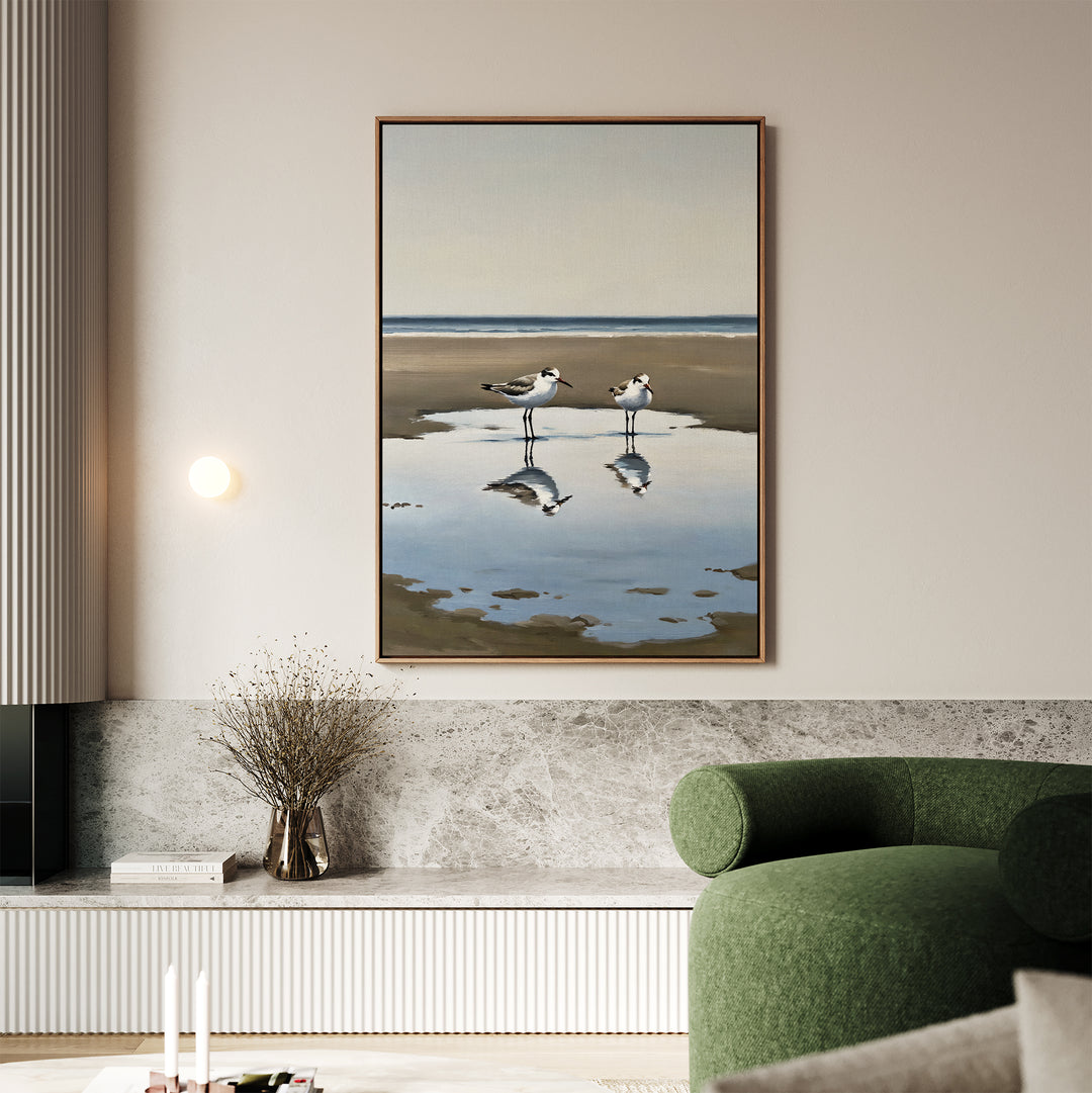 A modern living room with a green chair, marble accents, and the Drifted Calm Canvas Art—a large framed painting of two shorebirds by the water—brings elegant coastal inspiration to contemporary interiors.