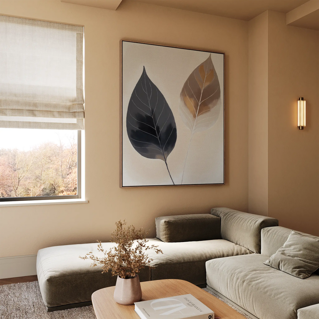 A modern living room with a beige sectional sofa, wooden coffee table with dried flowers, large Dual Leaf Study Canvas Art on the wall, and a window with beige Roman shades letting in natural light.