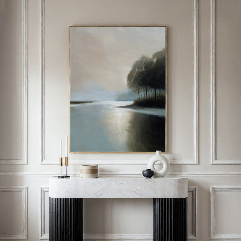 A minimalist console table with decorative objects stands against a paneled wall, above which hangs the Dusklake Canvas Art—a framed painting of a serene lakeside landscape in soft, muted tones.