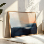 Dusk Ridge Canvas Art, a framed abstract landscape in soft blue, white, and peach tones, rests against a white wall in a sunlit room. Light streams in, casting tranquil shadows—perfect for creating a serene bedroom atmosphere.