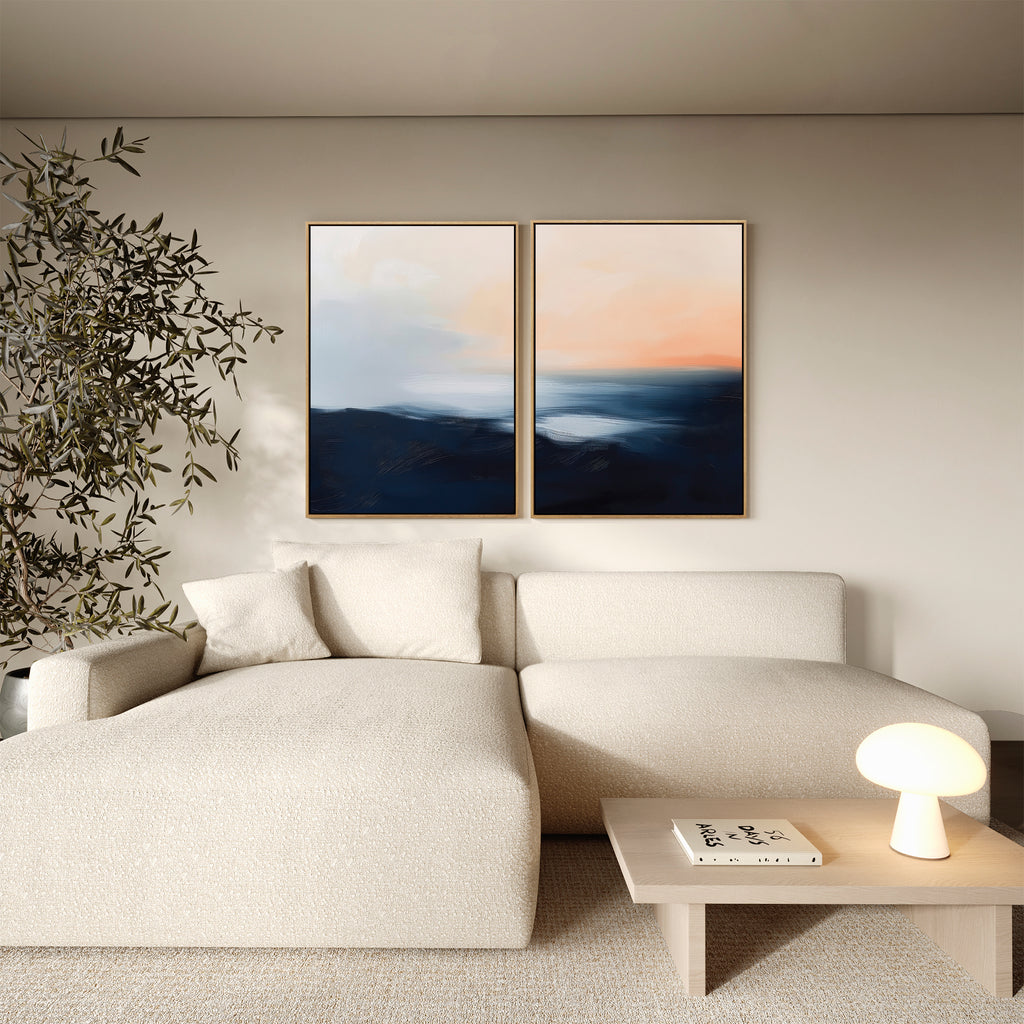 A modern living room with a cream sofa, a small wooden coffee table, a large leafy plant, and the Dusk Ridge Set of 2—abstract landscape paintings in blue and peach tones—adds a calming touch to the space.