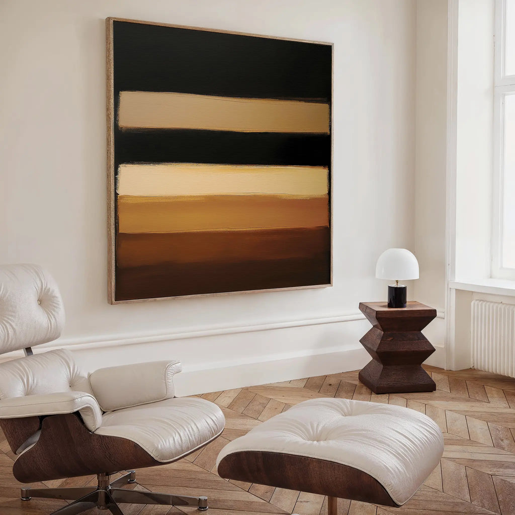 A modern living space with a white leather lounge chair and ottoman, a geometric wooden side table with a small lamp, and the Earth Layers Canvas Art featuring horizontal bands of brown, beige, and black on the wall.