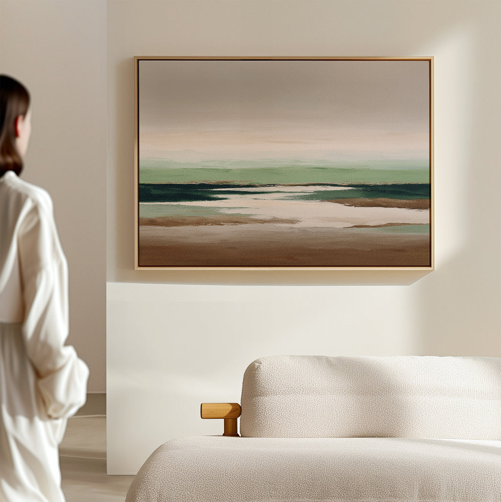 A person stands in a minimalist room, admiring the Earthbound Horizon Canvas Art—a striking abstract landscape with earthy tones and soft greens—displayed above a light-colored textured sofa.