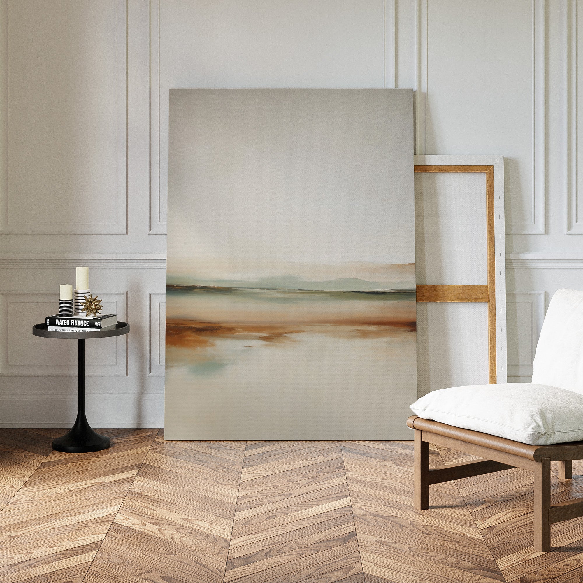 A minimal, modern living room decor with herringbone wood floors, a white cushioned chair, black side table with candles and books, and the Earthly Hues Abstract Canvas Art—a striking abstract landscape—leaning against the wall.