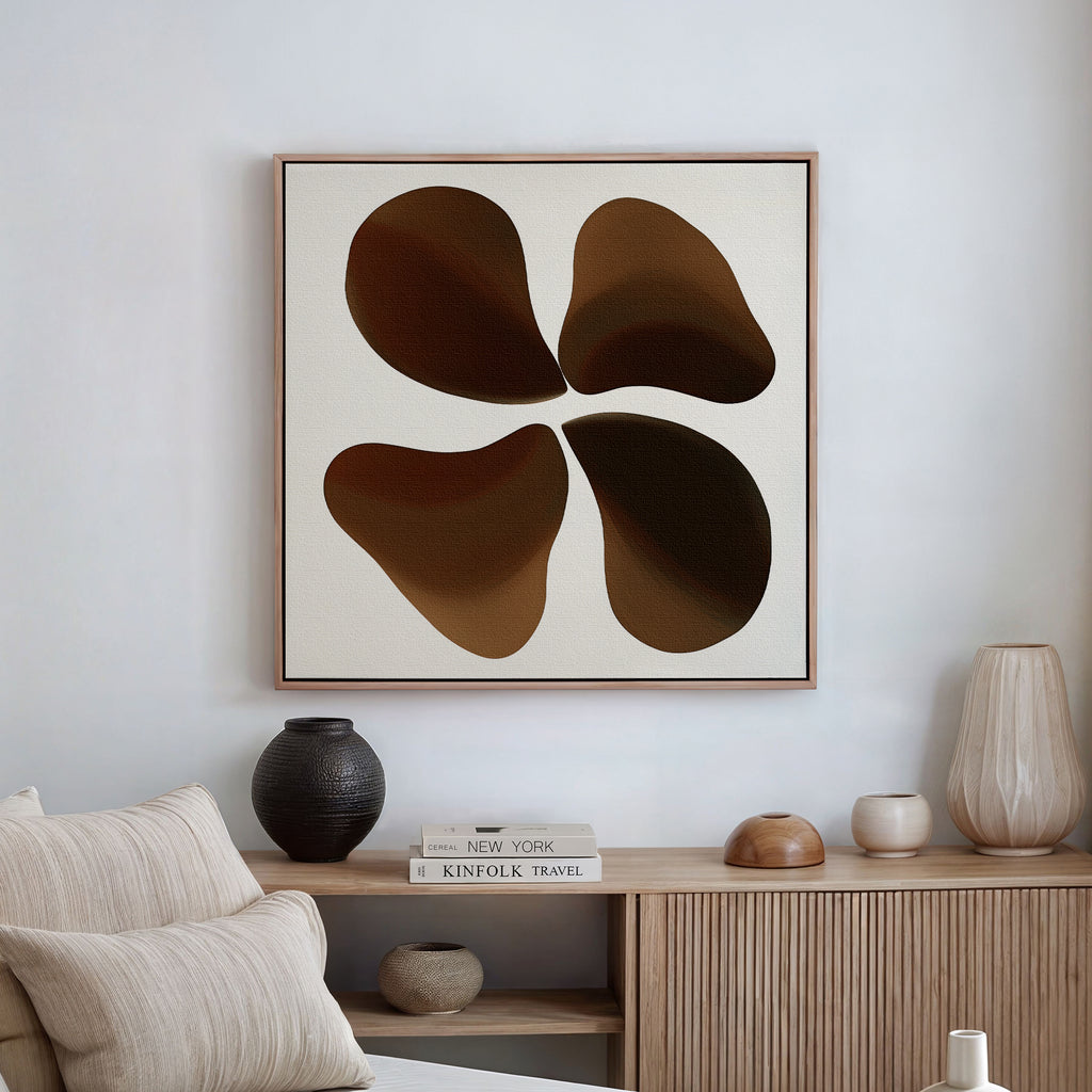 A modern living room with neutral decor features a beige sofa, light wood sideboard, vases, and Earthy Blooms Canvas Art—a minimalist piece with four overlapping brown shapes on a white background.