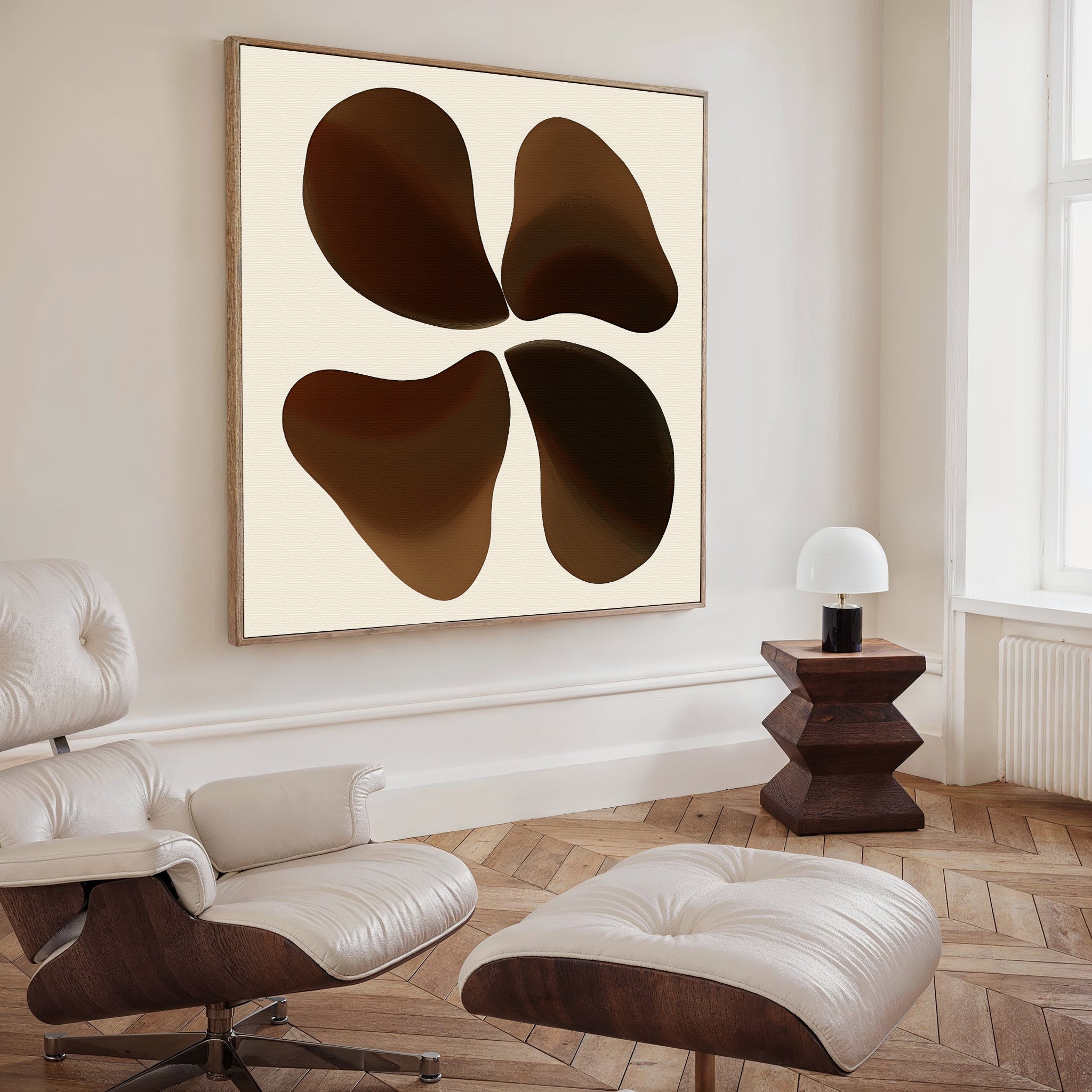 A modern, minimalist living room features a white lounge chair with ottoman, wooden side table and lamp, and large Earthy Blooms Canvas Art displaying four brown organic shapes. A light wood herringbone floor adds warmth to the space.