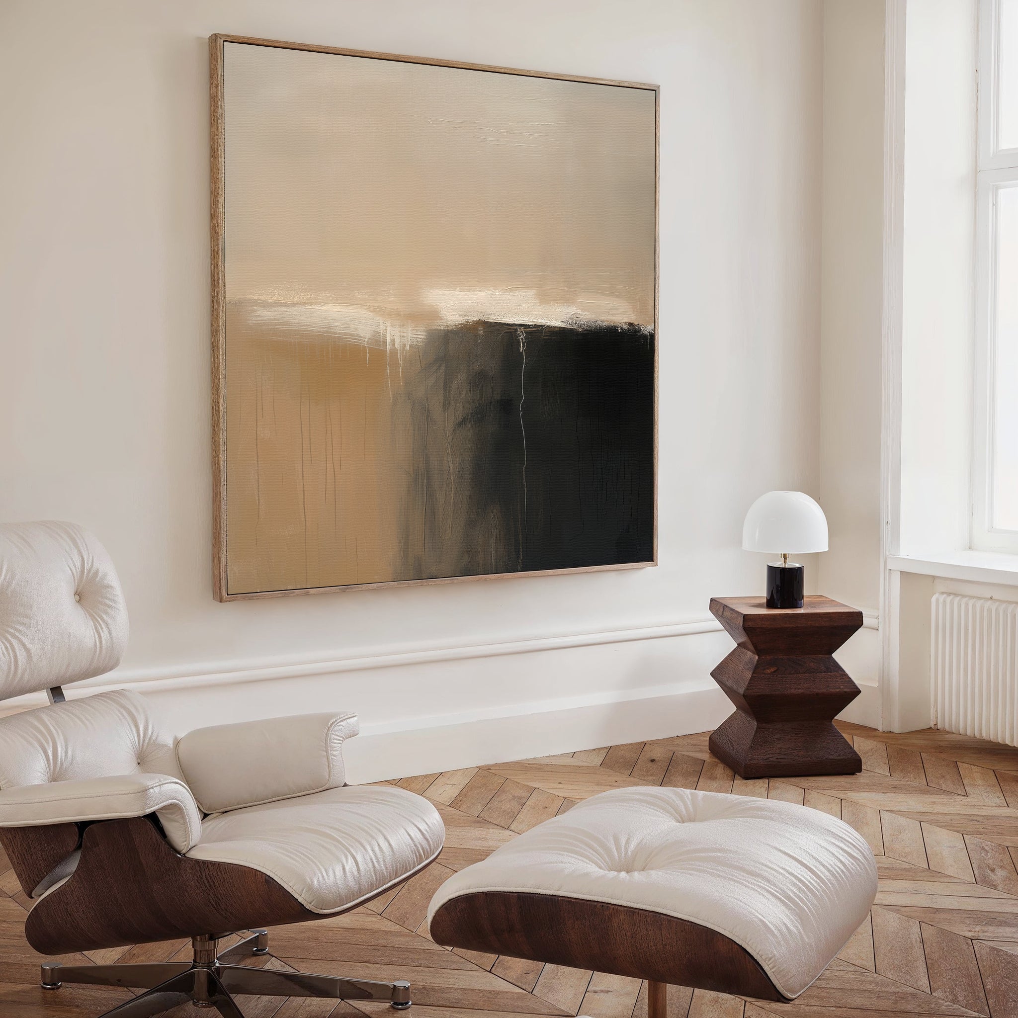A modern living room features a cream leather lounge chair and ottoman, herringbone wood floors, a dark wood side table with a white lamp, and is accented by the Earthy Cliffs Abstract Canvas Art for a chic, minimalist touch.