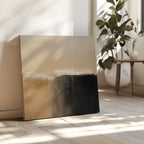 The Earthy Cliffs Abstract Canvas Art, with beige and black tones, leans against a sunlit wall on a wooden floor, complementing your living room decor near a green plant and a small table with a vase.