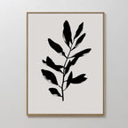 The Ebony Leaf Canvas Art showcases a black leafy branch silhouette on a light beige backdrop, set in a slim gold frame—stylish botanical wall decor ideal for enhancing modern interiors.