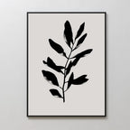 The Ebony Leaf Canvas Art features a minimalist black leafy branch with bold shapes on a light beige background. Framed in a thin black frame, it brings subtle elegance and modern style to any interior.
