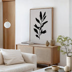 A minimalist living room featuring a light wood sideboard, Ebony Leaf Canvas Art, neutral pottery, a small potted plant, and a white sofa with a plush cushion—perfect for modern interiors.