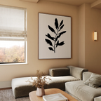 A modern living room with neutral tones features the Ebony Leaf Canvas Art—a large abstract black leaf—paired with a beige sectional, wooden coffee table with dried flowers, and a roman shade, perfect for stylish contemporary interiors.