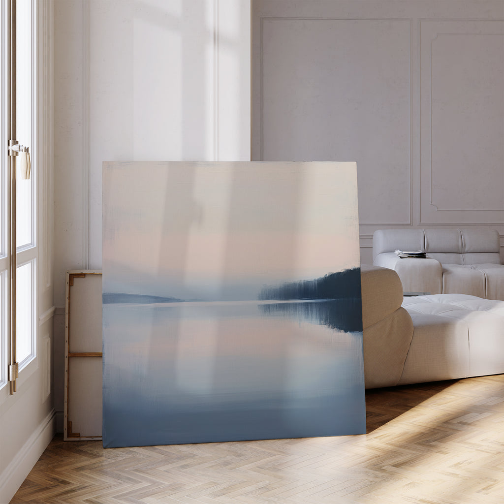 The Echo Lake Canvas Art, depicting a tranquil lake and distant trees, leans against the wall of a bright modern living room with light walls, a white sofa, and wooden parquet floors.