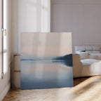 The Echo Lake Canvas Art, depicting a tranquil lake and distant trees, leans against the wall of a bright modern living room with light walls, a white sofa, and wooden parquet floors.
