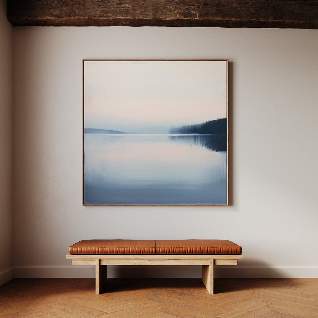 A minimalist room features a wooden bench with a brown leather cushion below Echo Lake Canvas Art, a large framed lake scene with soft blue and pink tones, hanging on a light-colored wall.