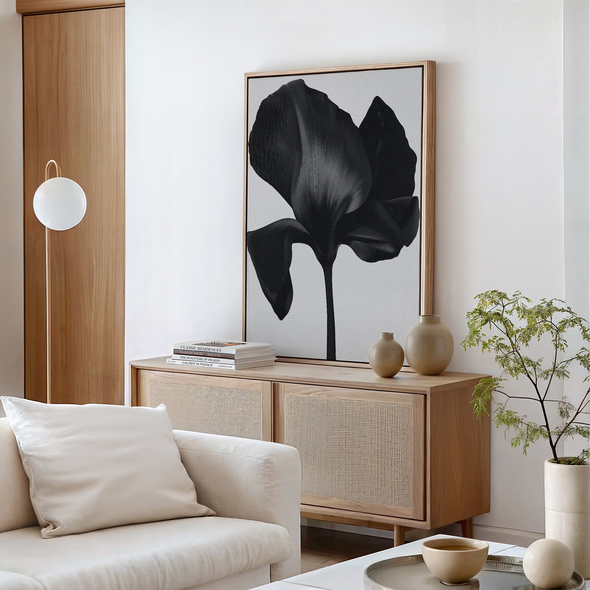 Minimalist living room with a light wood sideboard, Eclipse Bloom Canvas Art featuring large black-and-white flowers, neutral vases, a small green plant, and a white sofa with a beige pillow—perfect for stylish decor.
