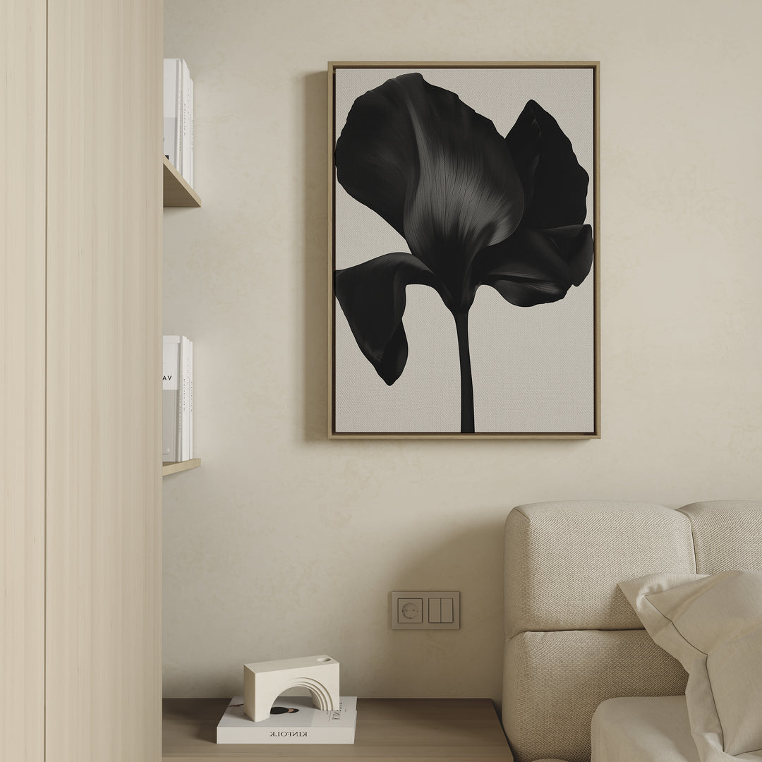 Minimalist living room featuring a beige sofa, light wood shelves with books, and the Eclipse Bloom Canvas Art—a large black abstract flower print—above an outlet. A small decorative object completes the stylish decor.