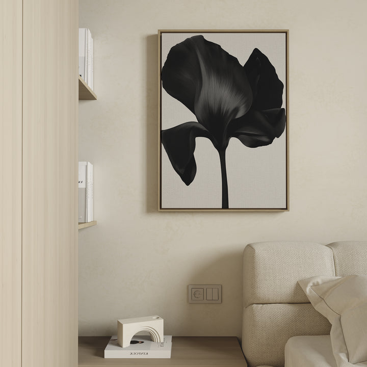 Minimalist living room featuring a beige sofa, light wood shelves with books, and the Eclipse Bloom Canvas Art—a large black abstract flower print—above an outlet. A small decorative object completes the stylish decor.
