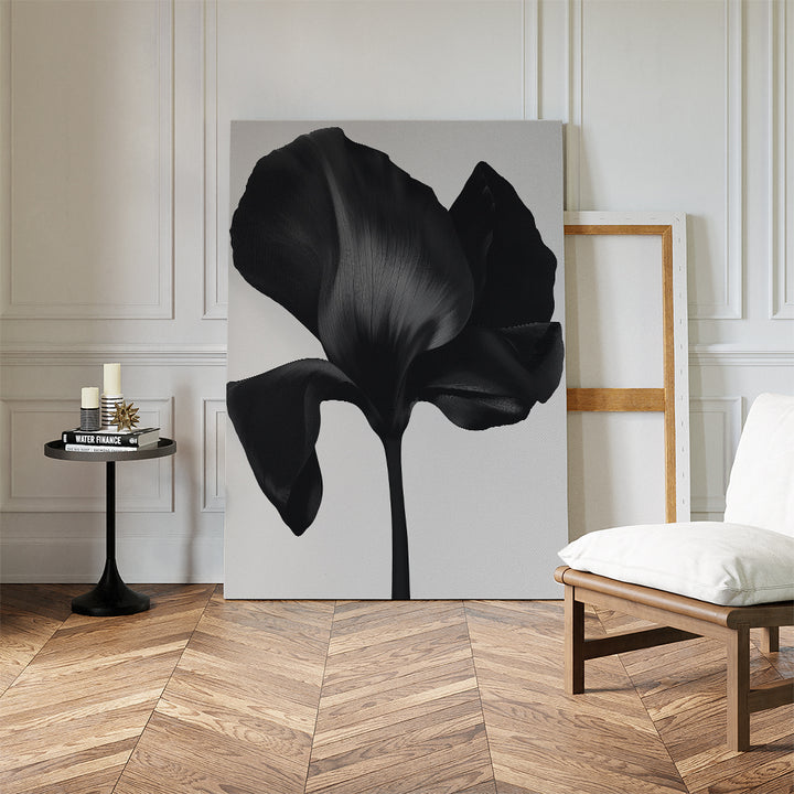 A modern living space with herringbone floors, a white cushioned chair, black side table, and minimalist décor featuring the Eclipse Bloom Canvas Art—a large black floral artwork—leaning against a white-paneled wall.