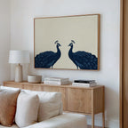 A minimalist living room with a wooden sideboard, white lamp, ceramic bowl, books, and the Elegant Plumage Canvas Art—featuring two blue peacocks on beige—an elegant choice for modern decor.