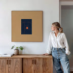 A woman in a white blouse and blue jeans leans against a wooden cabinet in a modern, minimalist room, admiring the Ember Point Canvas Art on the wall. A small plant and books add to the contemporary living room decor.