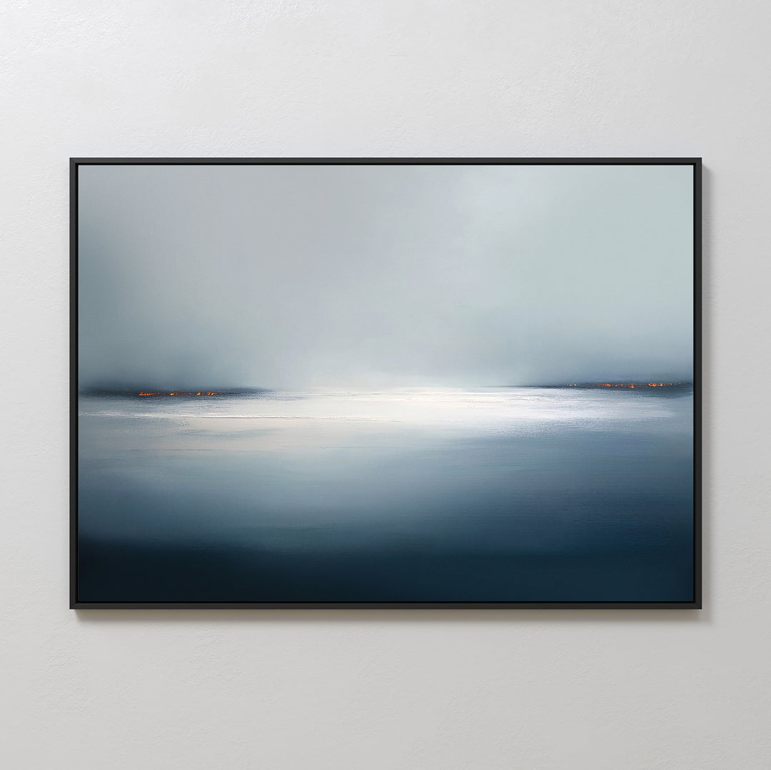 The Emberline Stillness Canvas Art – Horizontal is a framed abstract painting of a misty, blue-toned seascape with soft gradients and a bright center. Small orange dots on the horizon evoke distant lights, creating striking minimalist wall art on a white wall.